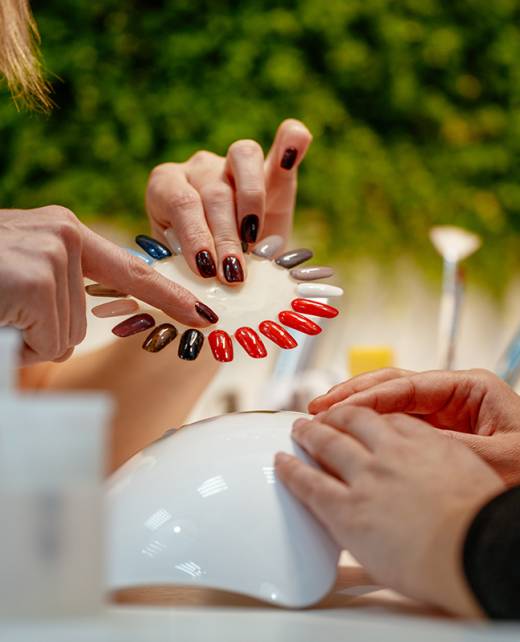 Close-up of a beautician and female clients hands holding samples and choosing colours nails at the beauty salon.